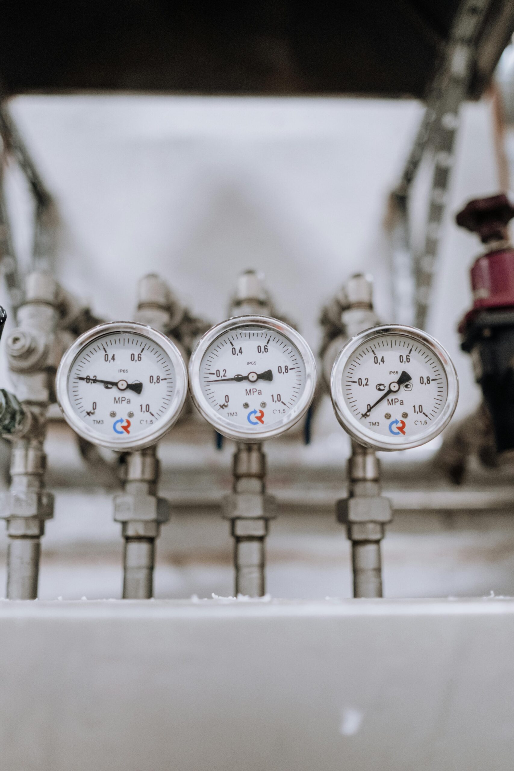 Close-up of three industrial pressure gauges on pipelines indoors.